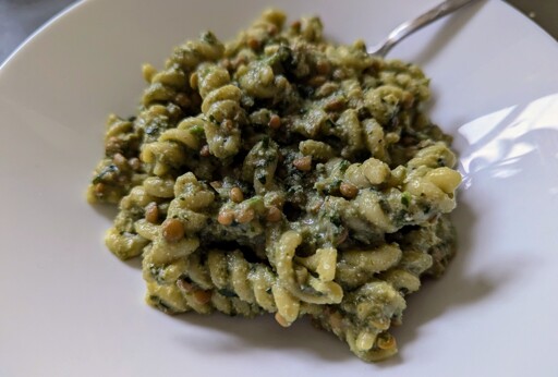 spiral pasta noodles covered in a green sauce on white plate.