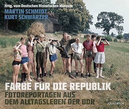 The book cover of "Farbe für die Republik" depicting eleven young people standing in what looks like a rural farm area. Some have binoculars and one is holding a large camera and pointing to direct all their attention toward something afar.